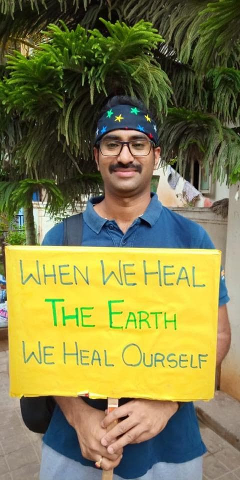 A volunteer holding a hand-painted placard reading “When we heal the Earth we heal ourself”