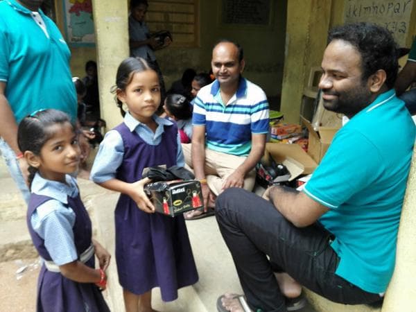 Two pupils in school uniform receiving a boxed school supply set on a veranda
