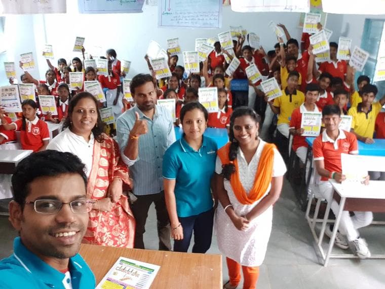 A classroom of students holding up printed career guidance booklets, with volunteers at the front